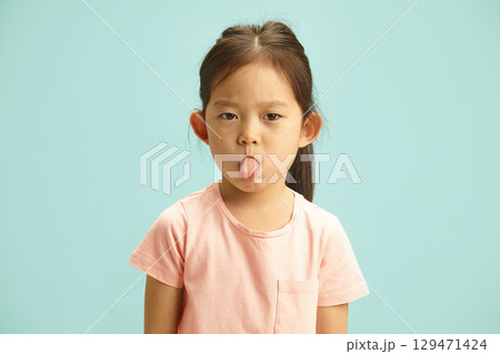 Mischievous Girl Making a Face, Sticking Out Her Tongue Showing to Camera, Studio Portrait Over Blue Isolated Mischievous Girl Making a Face, Sticking Out Her Tongue Showing to Camera, Studio Portrait Over Blue Isolated 129471424