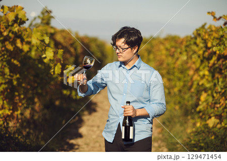 Asian Sommelier Tasting Red Wine in Sunlit Vineyard 129471454