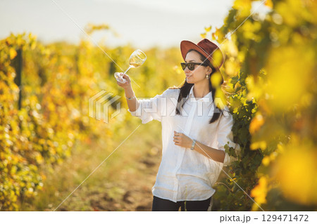 Female Sommelier Evaluating White Wine in the Midst of a Vineyard During Sunny Afternoon Female Sommelier Evaluating White Wine in the Midst of a Vineyard During Sunny Afternoon 129471472