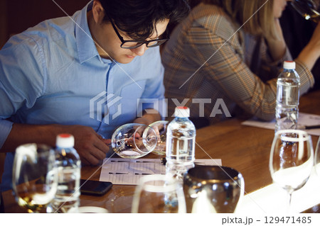 Man Analyzing White Wine at Table Participating in Sommelier Tasting 129471485