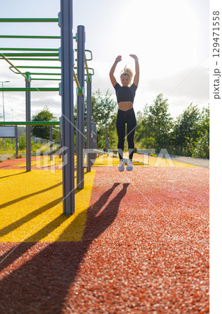 Woman Performing Jump Exercise at Outdoor Fitness Park on a Sunny Day 129471558