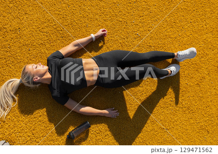 Athletic woman relaxing outdoors in activewear on vibrant textured surface 129471562