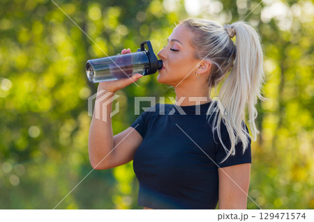 Woman outdoors drinking water from a bottle during a fitness activity Woman outdoors drinking water from a bottle during a fitness activity 129471574