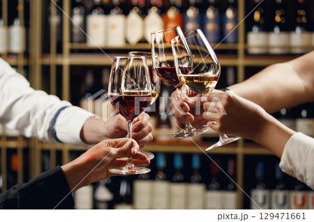 Big company people clinking glasses with red, rose and white wine on blurred cellar background. Men and women cheers with alcohol drink, closeup 129471661