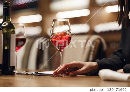 Female sommelier swirling red wine in glass on cellar background being in cellar. Wine expert exam to study different wine. Female sommelier swirling red wine in glass on cellar background being in cellar. Wine expert exam to study different wine. 129471662