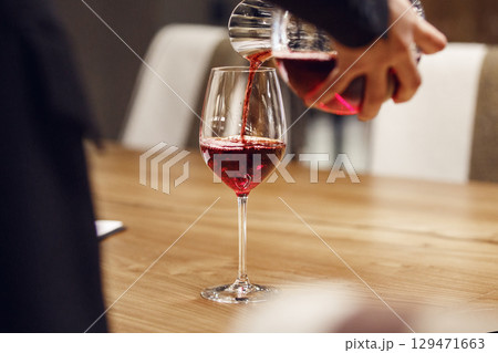 Bartender pouring red wine from decanter to the glass, close up image. 129471663