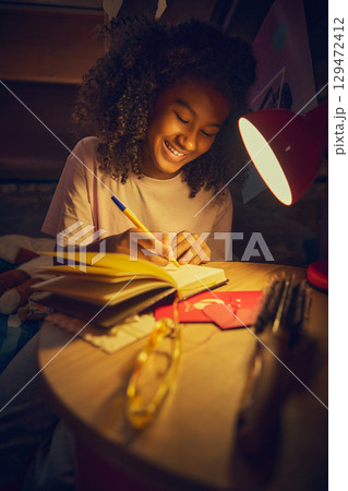 Teen girl smiling while writing in notebook under red lamp Teen girl smiling while writing in notebook under red lamp 129472412