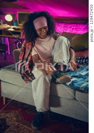 Smiling teen tying shoelaces in retro attic bedroom 129472450