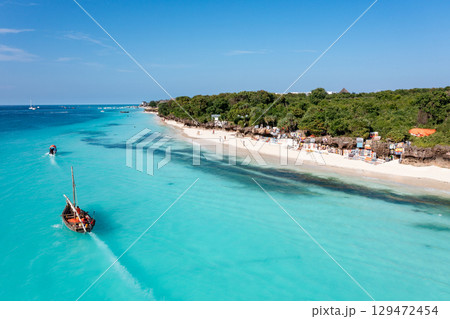 Zanzibar beach scene with dhow boats and tourists enjoying the turquoise water Zanzibar beach scene with dhow boats and tourists enjoying the turquoise water 129472454
