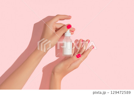 Womans hands holding dropper serum on pastel pink background. Self care beauty treatment concept 129472589