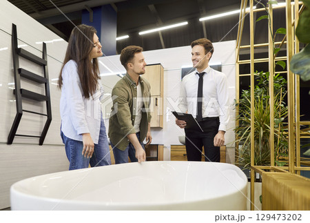 Couple choosing bathtub for bathroom in their house standing with salesman in bath store. 129473202