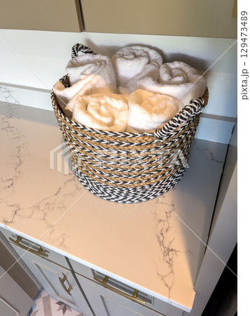 A round woven basket filled with rolled blankets placed on a marble kitchen counter. The light cabinetry and soft decor create a welcoming and homey atmosphere. A round woven basket filled with rolled blankets placed on a marble kitchen counter. The light cabinetry and soft decor create a welcoming and homey atmosphere. 129473489