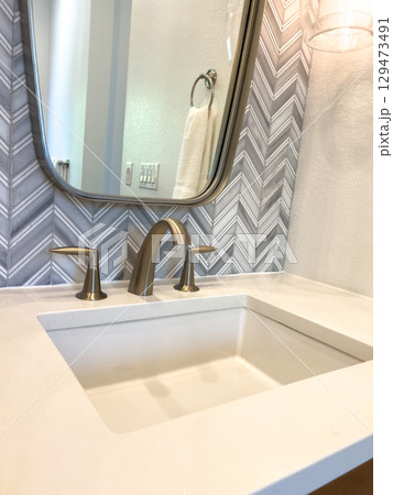Close-up of a bathroom vanity with a white sink, brushed nickel faucet, and curved mirror. Chevron wall tile and light tones create a bright, refined space. Close-up of a bathroom vanity with a white sink, brushed nickel faucet, and curved mirror. Chevron wall tile and light tones create a bright, refined space. 129473491