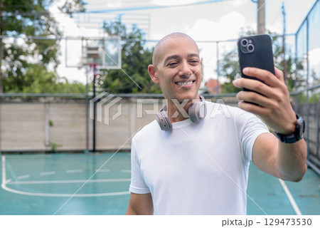 Latin man using smartphone on outdoor basketball court, urban sports fitness lifestyle 129473530