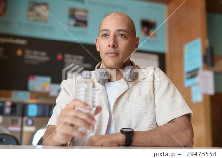 Bald Latin man drinking water in laundromat with washing machines behind Bald Latin man drinking water in laundromat with washing machines behind 129473558