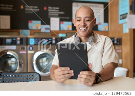 Latin man using digital tablet computer in laundromat with washing machines in background Latin man using digital tablet computer in laundromat with washing machines in background 129473562