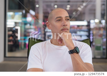 Bald Latino man sitting outdoors in coffee shop, confident summer portrait and wellness lifestyle 129473574