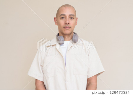Bald Latin man in casual shirt with headphones around neck against beige background Bald Latin man in casual shirt with headphones around neck against beige background 129473584