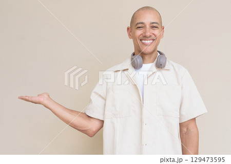 Confident bald Latin man in casual shirt with headphones around neck showing copy space 129473595