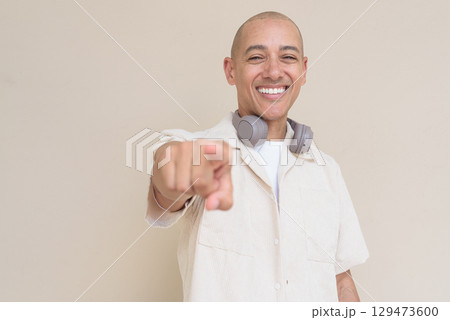 Bald Latin man in casual shirt with headphones around neck pointing finger at camera Bald Latin man in casual shirt with headphones around neck pointing finger at camera 129473600