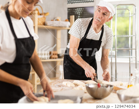 Elderly man and woman molding and cutting pieces of dough Elderly man and woman molding and cutting pieces of dough 129474034