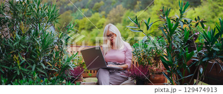 Banner of older woman working from homeoffice, sitting on terrace with laptop. Banner of older woman working from homeoffice, sitting on terrace with laptop. 129474913