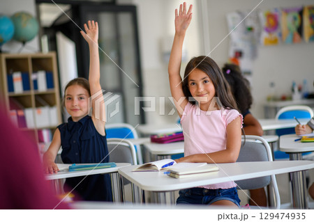 School children sitting at the desk in classroom on the lesson, raising hands. 129474935
