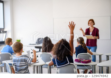 School children sitting at the desk in classroom on the lesson, raising hands. 129474942