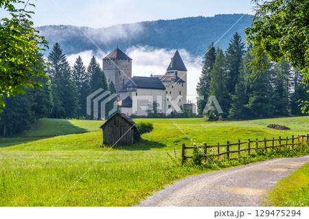 Mauterndorf Castle rises majestically amid lush green fields and towering trees. The misty backdrop adds a magical touch, inviting visitors to explore its rich history and stunning architecture. 129475294
