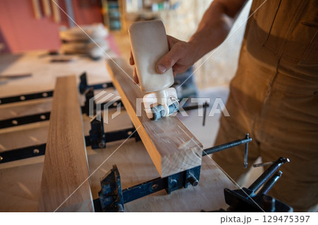 Joiner man hands gluing wooden beams before clamping forming solid board. Surface smooth, even coat 129475397
