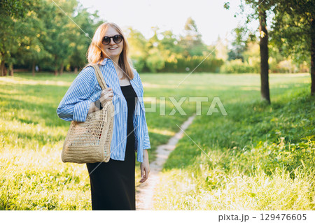 Young 30s blonde woman with bag smiling at the park. Lifestyle, fashion, people concept. 129476605