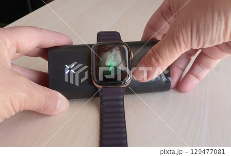 Woman charges her smart watch using portable wireless charger in room. Modern lifestyle, mobile technology, travel. Woman charges her smart watch using portable wireless charger in room. Modern lifestyle, mobile technology, travel. 129477081