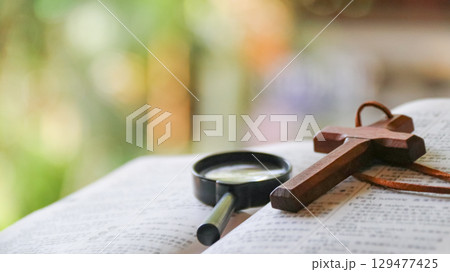 Wooden cross and magnifying glass on old book Wooden cross and magnifying glass on old book 129477425