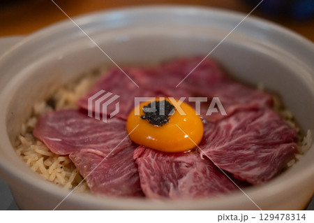 Beef fat fried rice in a bowl, with sliced meat and egg yolk on top 129478314