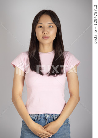 Woman is standing still and looking directly at the camera, with her hands clasped in front of her. 129478712