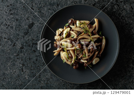 Fried shimeji mushrooms with thyme and garlic on a black plate. Fried shimeji mushrooms with thyme and garlic on a black plate. 129479001