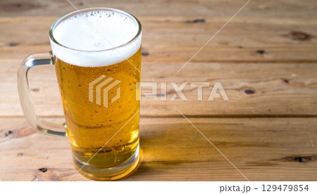 木製テーブルに置かれた霜付きグラスの黄金色ラガービールと白い泡のクローズアップ 129479854