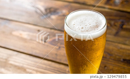 木製テーブルに置かれた霜付きグラスの黄金色ラガービールと白い泡のクローズアップ 木製テーブルに置かれた霜付きグラスの黄金色ラガービールと白い泡のクローズアップ 129479855