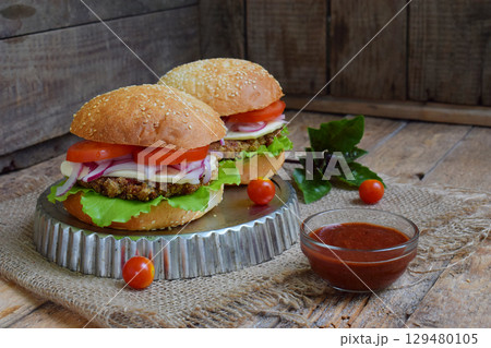 Veggie burgers with chop of eggplant, lettuce, pickled onions, tomato on a brown wooden background. Vegetarian lunch or dinner idea. Healthy food. Veggie burgers with chop of eggplant, lettuce, pickled onions, tomato on a brown wooden background. Vegetarian lunch or dinner idea. Healthy food. 129480105