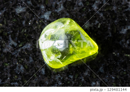 sample of tumbled peridod mineral on black granite 129481144