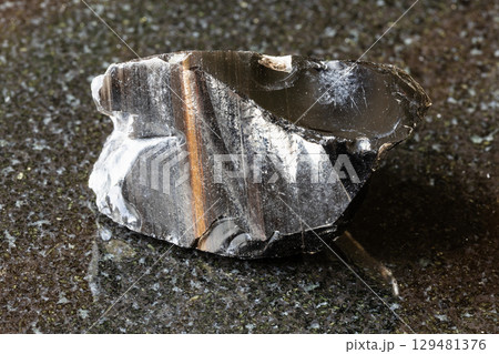 sample of raw striped obsidian mineral on black 129481376