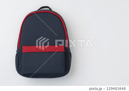 A navy blue backpack with a bold red front pocket is centered on a plain white surface. The design features a simple and modern aesthetic, suitable for school or travel use. 129481648