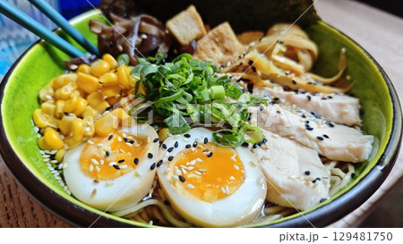 Bowl of ramen with soft boiled eggs, chicken slices, corn, green onions and sesame seeds in rich broth 129481750
