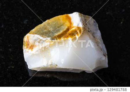 sample of raw white opal mineral on black granite 129481788