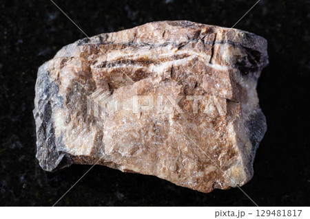 sample of raw rhodonite mineral on black granite 129481817