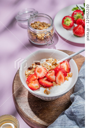 Granola or muesli with natural greek yogurt, strawberry and honey in a bowl on a wooden board 129482280