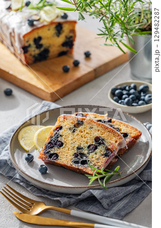 Pieces of homemade blueberry lemon cake on a plate on a light background with fresh berries 129482287