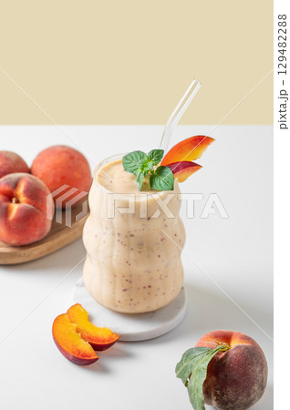 Smoothie with peach and banana in a glass on a marble stand on a yellow white background 129482288