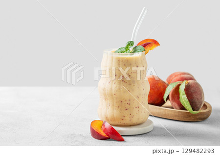 Smoothie with peach and banana in a glass on a marble stand on a light background Smoothie with peach and banana in a glass on a marble stand on a light background 129482293