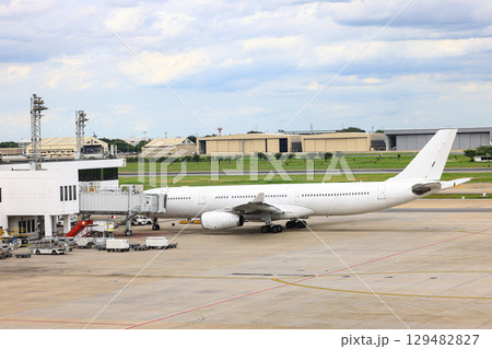 White commercial airplane parking at passenger gate, connect to gate with jet bridge. Being service by ground service team. 129482827